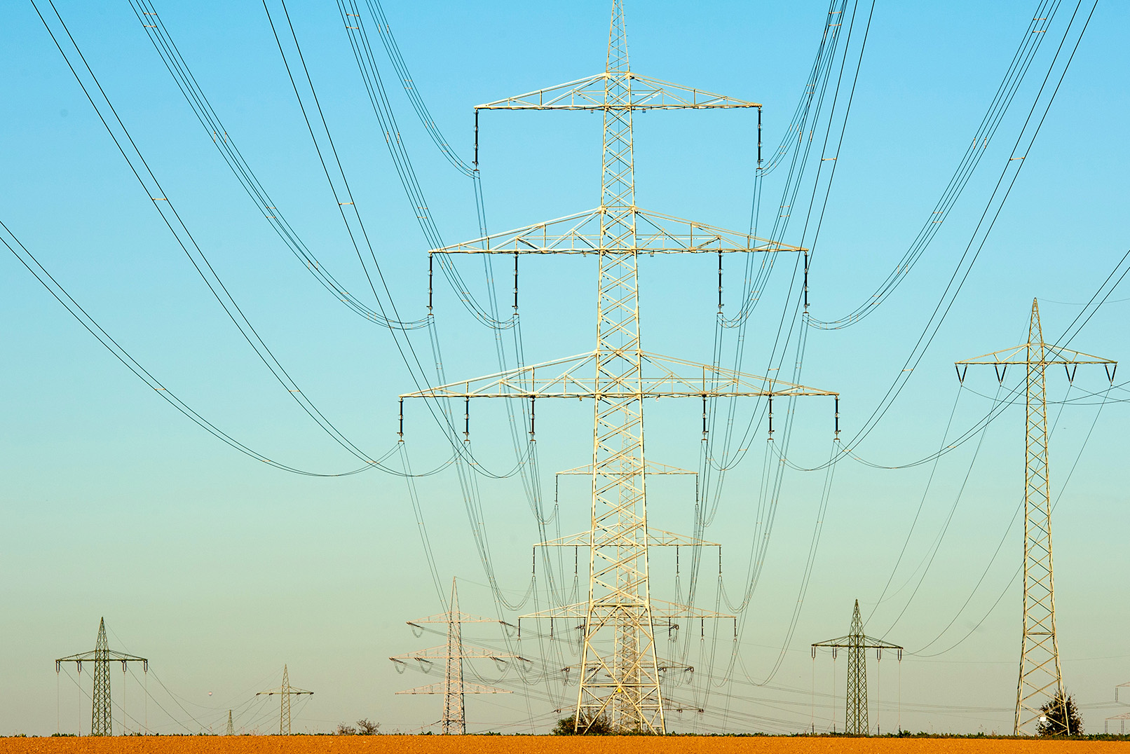 Large electricity pylon with three electricity pylons in the background with a bright blue coloured sky.